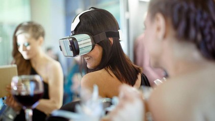 Eine Frau mit einer VR-Brille blickt ein Glas Wein an