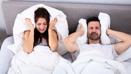 Paar im Bett kann aufgrund von Lärm nicht schlafen