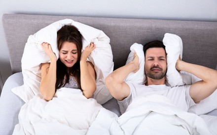 Paar im Bett kann aufgrund von Lärm nicht schlafen