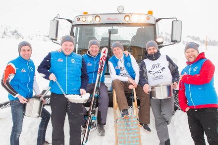 Sechs Köche mit Pfannen und Töpfen im Schnee vor einer Schneeraupe