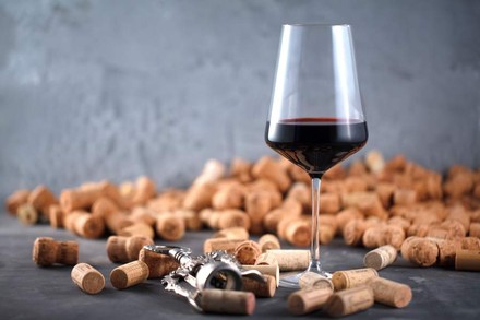 Ein halbvolles Glas steht inmitten mehrerer Weinkorken und einem Korkenzieher