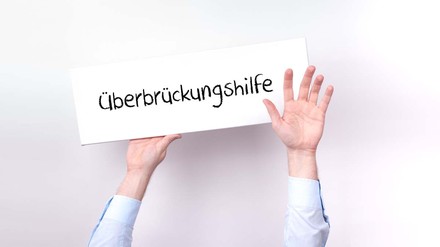 Hände heben Überbrückungshilfe-Schild in die Luft