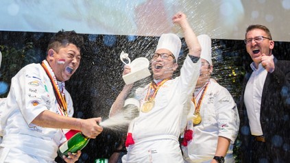 Köche feiern auf der Bühne mit einer Flasche Sekt