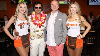 Zwei weibliche Servicekräfte der neuen Hooters-Filiale auf der Reeperbahn stehen neben zwei Männern von denen einer als Elvis verkleidet ist