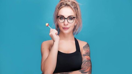 Eine junge, tattoowierte Frau mit einem Lolli in der Hand