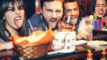 Eine Gruppe junger Menschen sitzt an der Bar, trinkt und sie strecken lachen ihre Zungen heraus