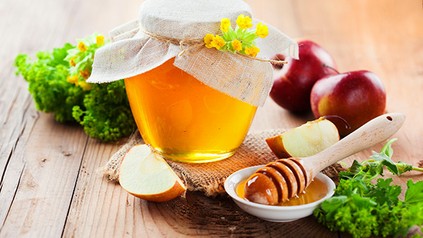 Ein liebevoll dekoriertes Gläschen in dem sich eine orangene Flüssigkeit befindet, daneben Honig Äpfel und Sellerie