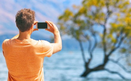 Mann fotografiert Baum in einem See mit dem Handy