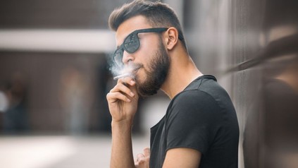 Junger bärtiger Mann mit Sonnenbrille raucht Zigarette