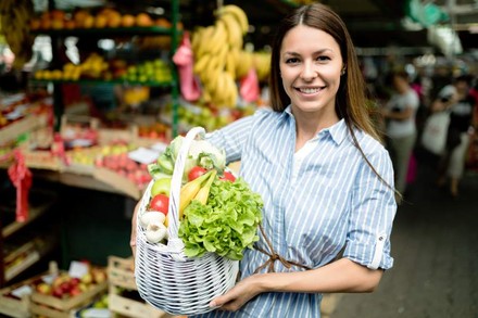 Eine junge Frau hält einen Korb mit diversem GEmüse und Obst