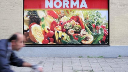 Ein Plakat von Norma mit diversem Gemüse und Obst an einer Hauswand