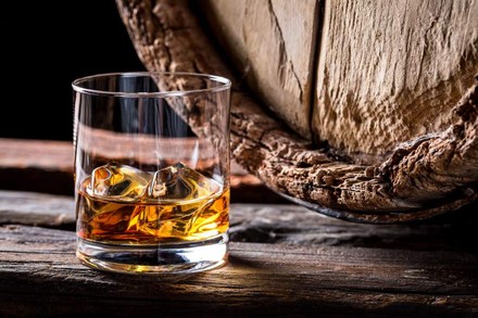 Ein Glas mit Whiskey und Eiswürfeln vor einem Holzfass