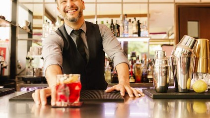 Ein grinsender Barkeeper stellt einen Drink auf den Tresen