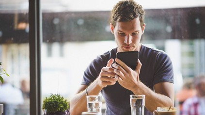 Junger Mann sintzt in einem Lokal und schaut auf sein Handy
