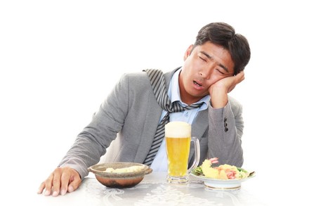 Müder Asiate sitzt vor Bier und Essen