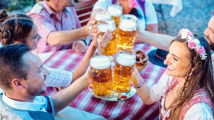 Grupper junger Leute in Dirndl und Lederhosen stoßen mit Bier-Maßkrügen an