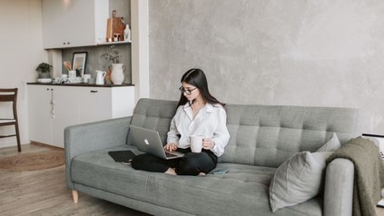 junge FRau mit Laptop sitzt auf einer Couch