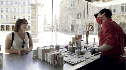 Würstelstand-Besucherin und -Mitarbeiter mit Mund-Nasenschutz