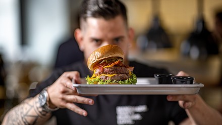 Ein Mann bringt einen Burger auf einem Tablett an einen Tisch.