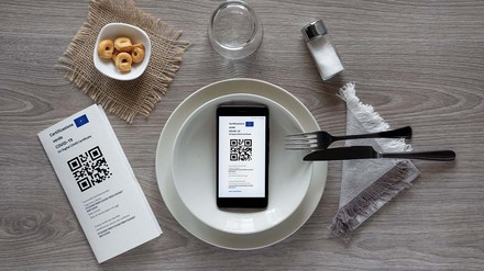 Auf dem Teller eines eingedeckten Platzes liegt ein Handy mit geöffnetem Impfausweis