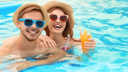 Ein Mann und eine Frau im Pool lachen in die Kamera. Die Frau hält einen Cocktail in der Hand.