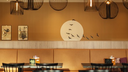 In Erdtönen gehaltener Essbereich im the niu Sparrow in Regensburg, an dessen Wand ein Vogelschwarm vor einer hellen Sonne gemalt ist