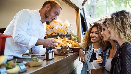 Foodtruck-Betreiber gibt Essen an drei junge Frauen aus