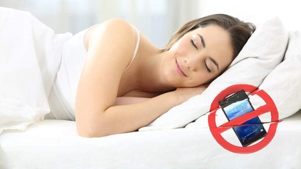 Eine Frau schläft entspannt auf einem Bett, auf dem ein Handyverbotszeichen zu sehen ist