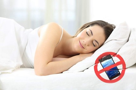 Eine Frau schläft entspannt auf einem Bett, auf dem ein Handyverbotszeichen zu sehen ist