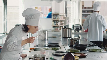 Eine Frau steht am Herd und probiert eine Soße.