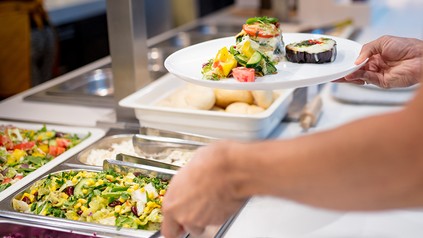 Jemand holt sich Essen von einer Mensatheke.