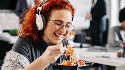 Eine Frau hat Kopfhörer auf und isst einen Salat.
