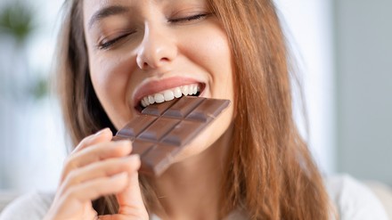 Eine Frau beißt genüsslich in eine Tafel Schokolade.