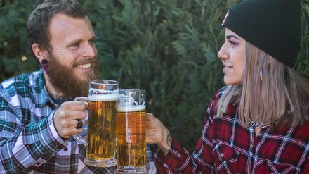 Ein junges Pärchen sitzt im Biergarten und prostet sich mit einem Bier zu.