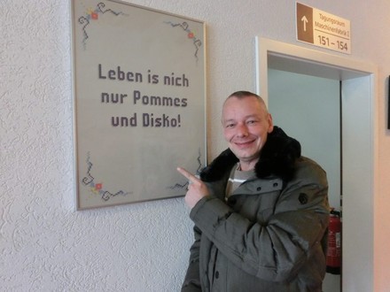 Harry Schulz zeigt auf Tafel mit Inschrift: „Leben ist nich nur Pommes und Disko!“