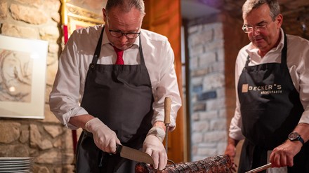 Christian Keiser (l) und Arno Milde vom Spießbratenclub Trier schneiden den Spießbraten in Portionen für die Clubmitglieder.