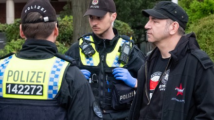 Der Fernsehkoch Ole Plogstedt steht bei einer Versammlungsauflösung neben Polizisten, die Personalien überprüfen. Aktivisten der Klimagruppe Letzte Generation wurden von Polizisten vor dem Hamburger Michel gestoppt.