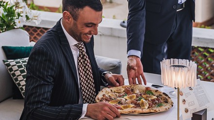 Ein Mann in Anzug bekommt eine Pizza serviert.