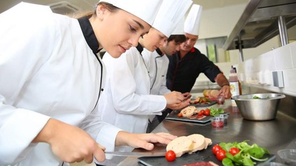 Drei junge Köche kochen unter der Anleitung ihres Ausbilders