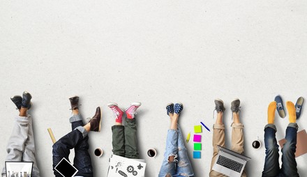 Mehrere junge Menschen strecken entspannt die Beine aus während ihre Arbeitsmaterialien neben ihnen liegen