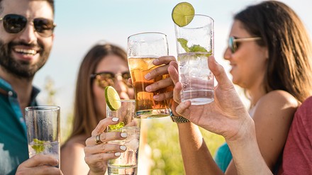 Eine Gruppe Erwachsener stößt bei Sonnenschein mit ihren Getränken an.