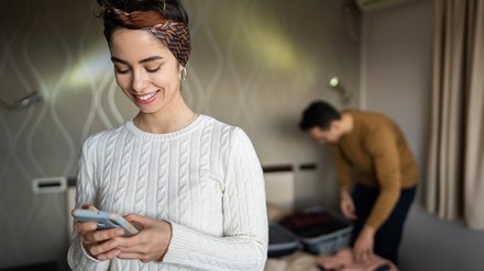Frau schaut in einem Hotelzimmer auf ihr Handy.
