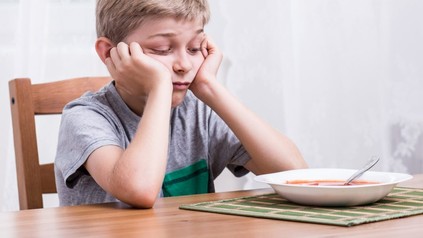Kind sitzt enttäuscht vor seiner Suppe