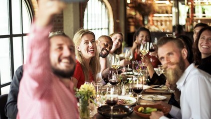 Eine Gruppe glücklicher Menschen sitzt zusammen beim Essen an einem Tisch und macht ein Selfie