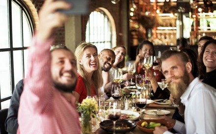 Eine Gruppe glücklicher Menschen sitzt zusammen beim Essen an einem Tisch und macht ein Selfie
