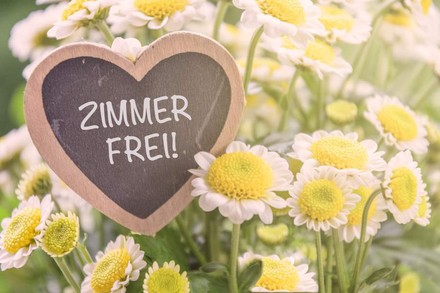 Ein herzförmiges Schild auf dem Zimmer Frei! steht steht in einer Blumenwiese