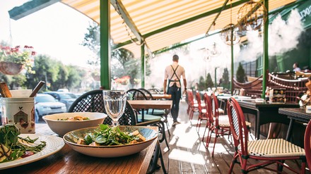 Restaurant mit Kellner in der Rückenansicht und im Vordergrund ein Teller mit Salat.