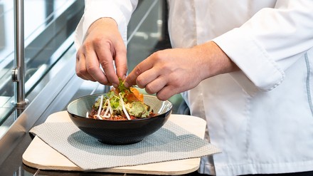 Ein Koch in weißer Haube richtet einen Salat an
