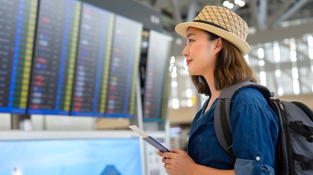 Junge Asiatin am Flughafen mit Ticket in der Hand