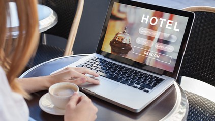 Frau bucht ein Hotelzimmer an ihrem Laptop und trinkt dabei einen Kaffee